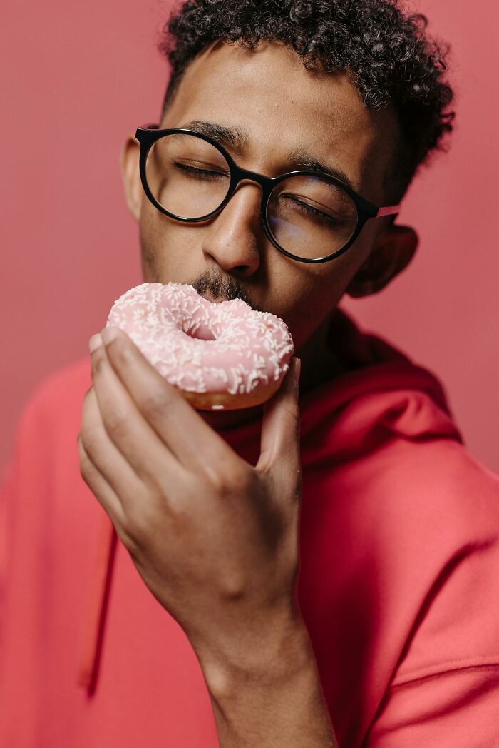 Man in glasses and red hoodie enjoying a pink frosted donut, reflecting on self-respect in relationships and partner dynamics.