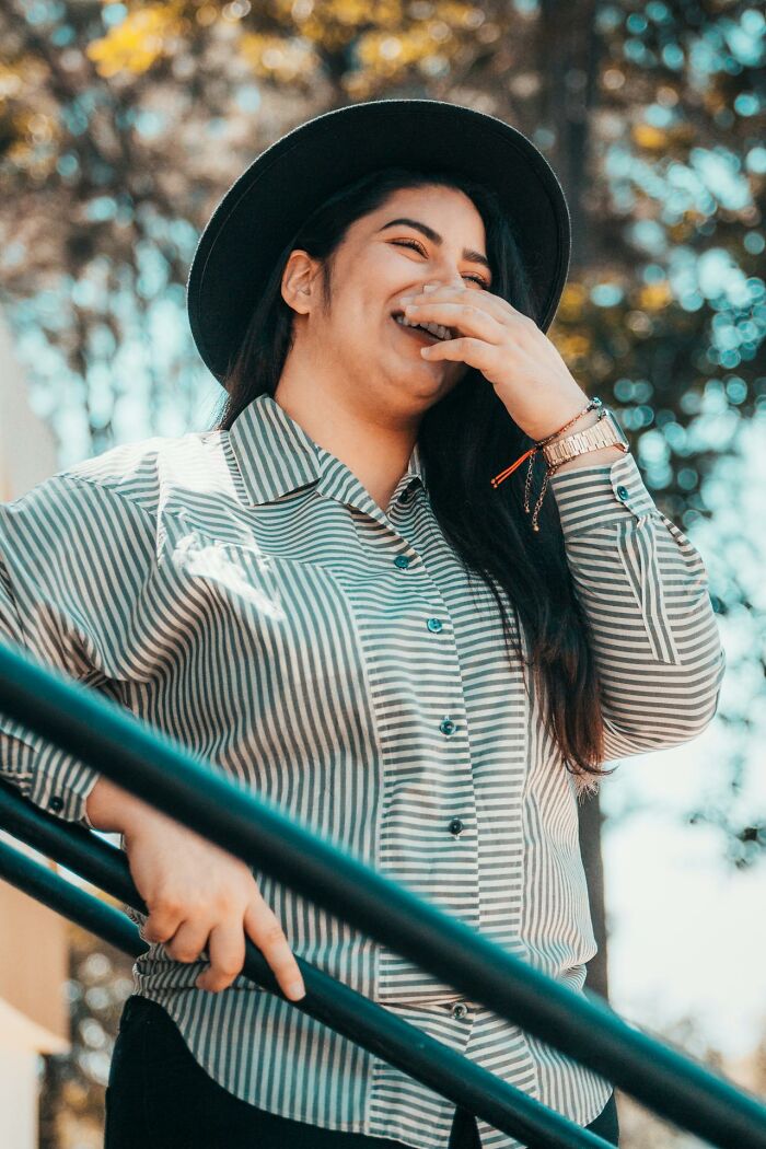 Young woman wearing a hat laughing outdoors, representing women listed in unhinged and toxic ways they traumatized men.