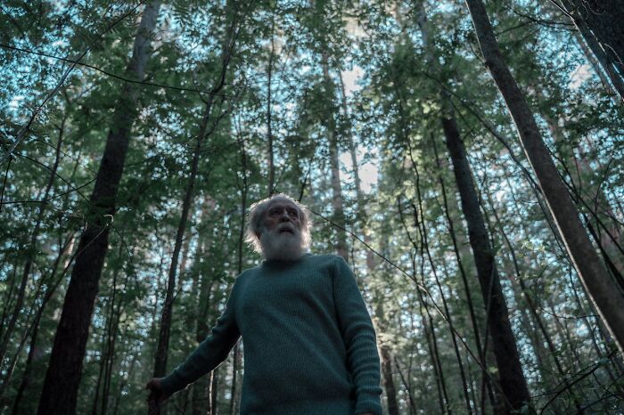 Elderly man looking alert in dense forest, capturing the chilling sounds that signal immediate disaster atmosphere.