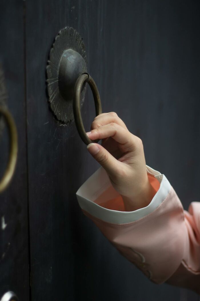 Hand gripping a metal door knocker on a dark door, evoking the chilling sounds signaling immediate disaster.