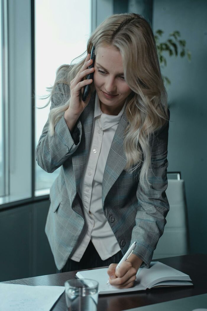 Woman in gray blazer taking notes while on a phone call, illustrating ideas for today I learned facts to use in conversations.