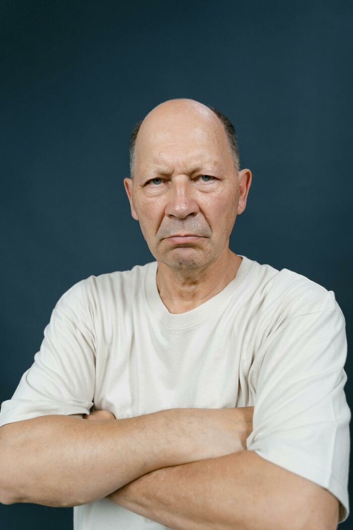 Older man with arms crossed and a serious expression, illustrating times people said stupid things causing long pauses.