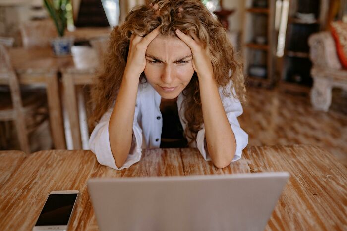 Woman concentrating intensely on a difficult 30-question hard general knowledge quiz on her laptop at a wooden table.