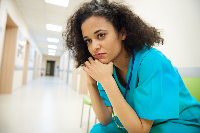 Young woman in medical scrubs sitting alone in hallway, looking pensive and worried, reflecting photo mother elderly cheating. Young woman in medical scrubs sitting alone in hallway, looking pensive and worried, reflecting photo mother elderly cheating.