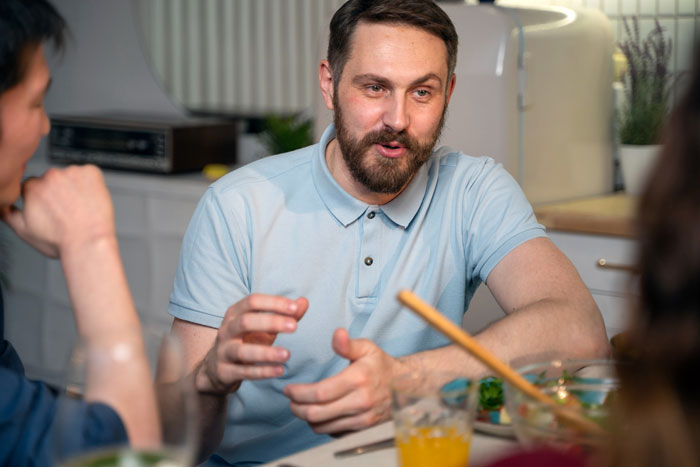 Man in a light blue shirt discussing relationship issues and bullying with friends at a dining table. Man in a light blue shirt discussing relationship issues and bullying with friends at a dining table.