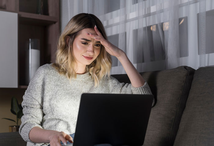 Woman looking worried at laptop screen, feeling gullible after taking boyfriend's prank about FBI seriously.