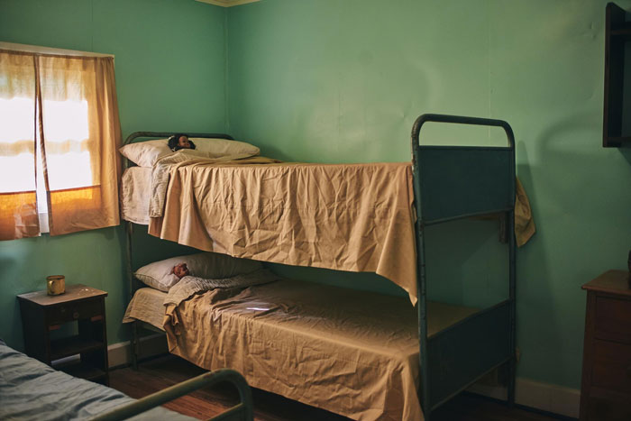 Two women resting on bunk beds inside a simple room at a homeless shelter, highlighting support for pregnant sister needs.