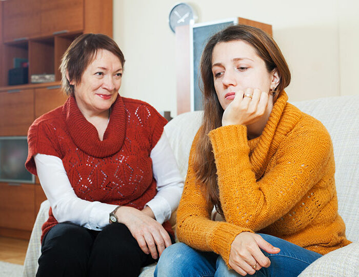 Pregnant woman looking uncomfortable and upset while sitting next to an older woman in a home setting.