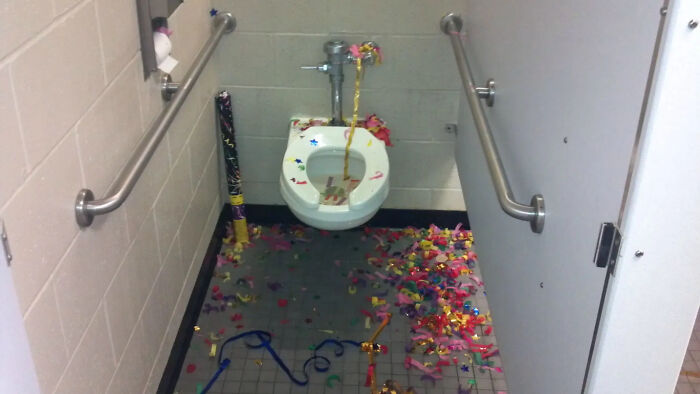 Public restroom toilet with colorful confetti and party streamers scattered on the floor and inside the bowl, funny photo.