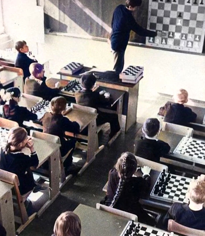 Children in a classroom learning chess from an instructor using a large board in a rare and intriguing history photo.