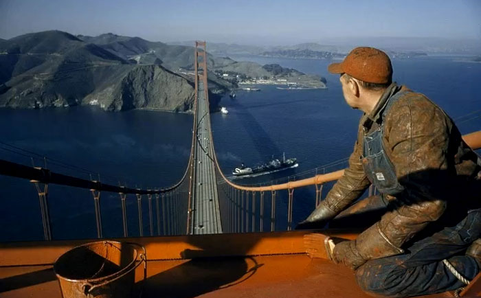 Construction worker overlooking the Golden Gate Bridge during its building phase in rare and intriguing historical photo.