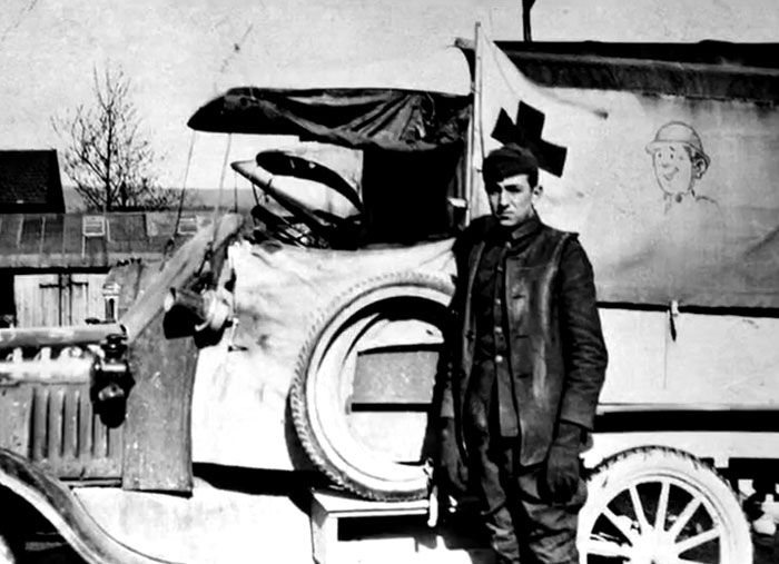 Black and white rare history photo of a soldier standing next to an old military vehicle from the early 20th century.