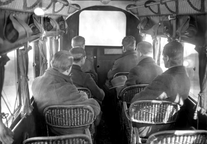 Interior of a vintage bus with men seated on wicker chairs, a rare and intriguing photo capturing history between headlines.