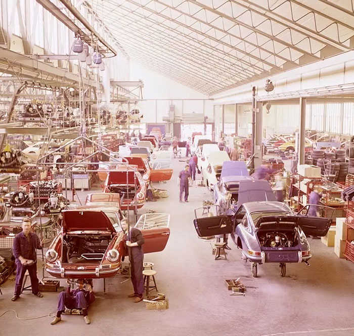 Vintage car factory with workers repairing and assembling vehicles in a rare and intriguing historical photo.