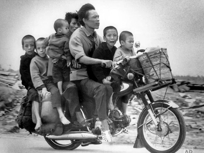 Black and white photo of a family of eight riding a single motorcycle, a rare and intriguing moment in history.