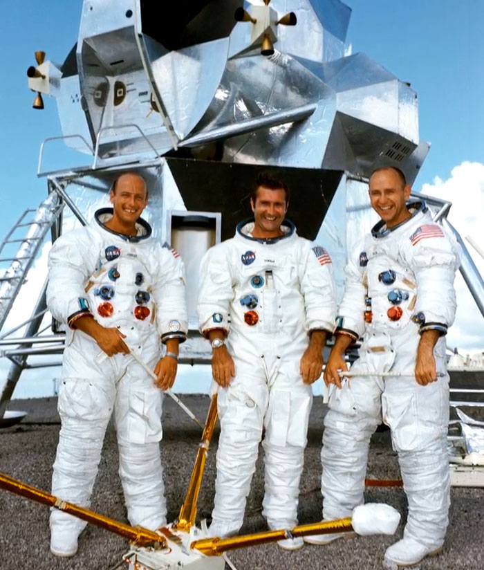 Three astronauts in space suits stand smiling in front of a lunar module in a rare and intriguing historical photo.