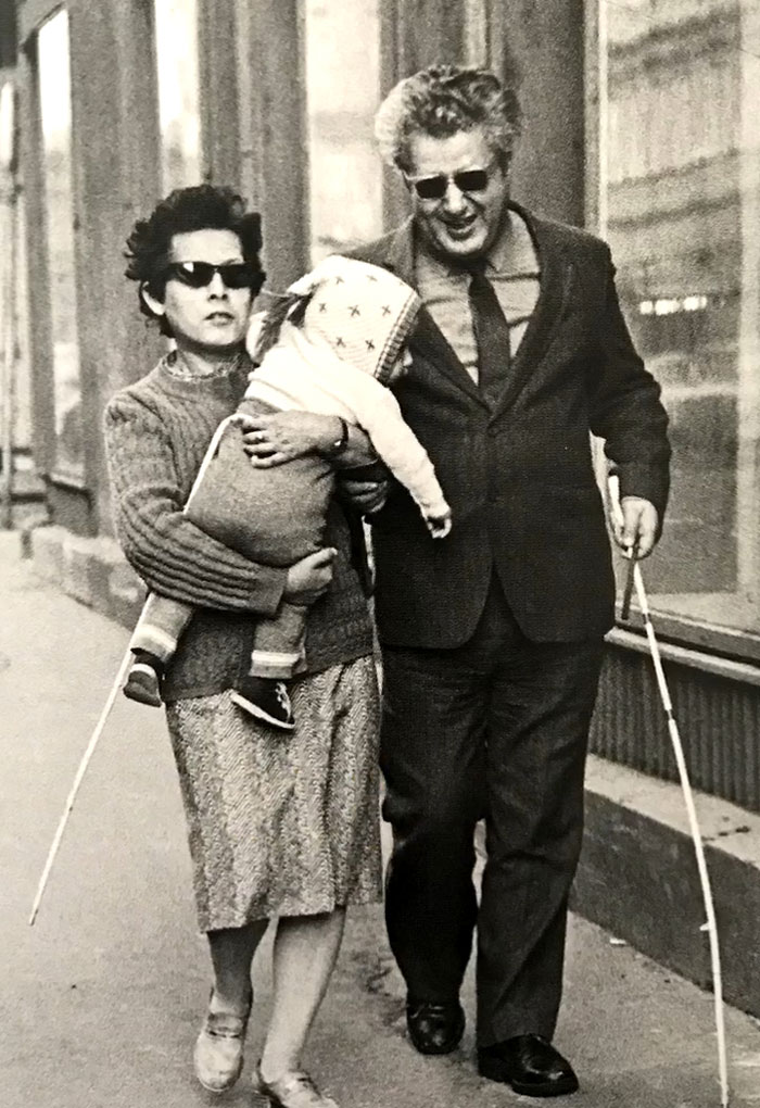 Black and white rare photo of a blind couple walking with a child using white canes, showing history between the headlines.