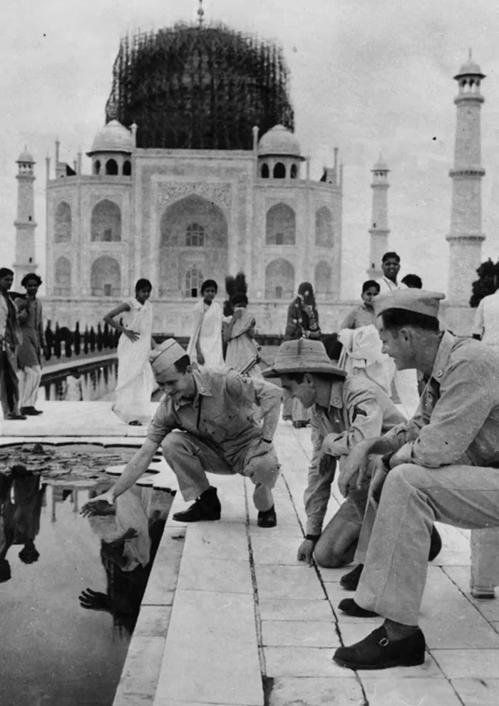 Black and white photo showing rare history moment of soldiers at Taj Mahal pool surrounded by local people and architecture.