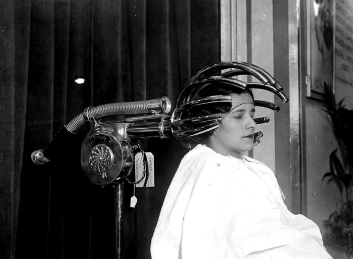 Woman using an early 20th-century hair drying machine in a rare and intriguing historical photo showing history between headlines.
