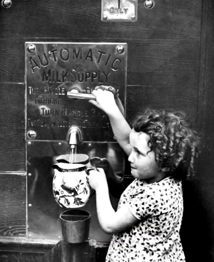 Young girl using an automatic milk supply machine in a rare and intriguing historical photo showing life between the headlines.