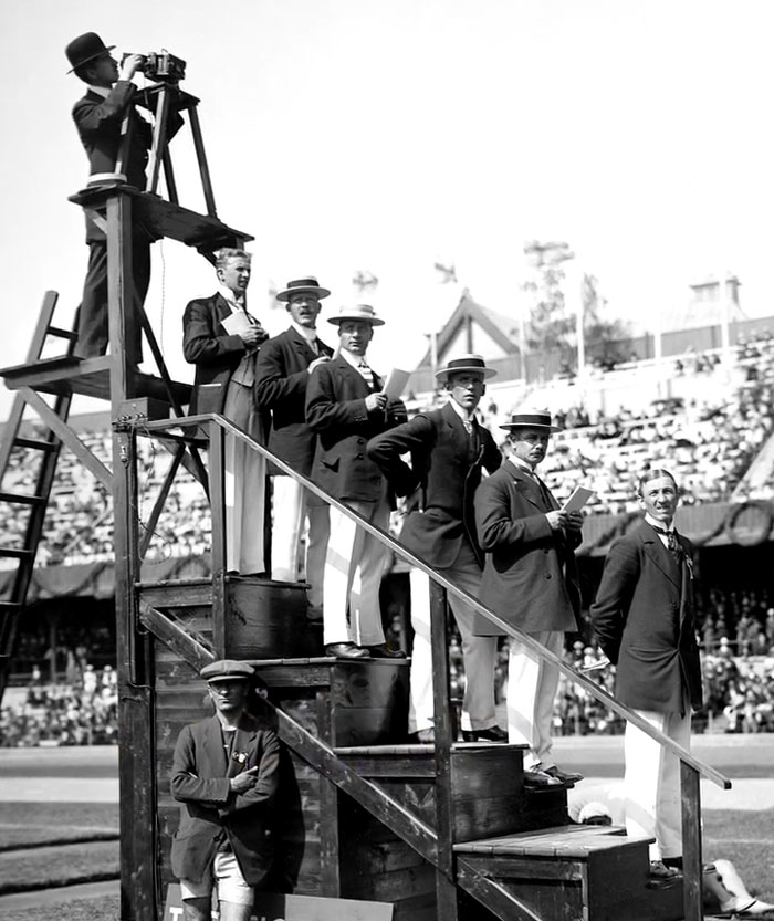 Group of men in early 1900s attire on a wooden platform, capturing rare and intriguing historical moments at a public event