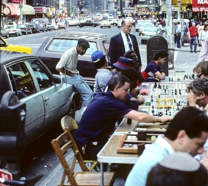 Street scene with multiple people playing chess outdoors in a busy urban area, showcasing rare and intriguing historical moments.