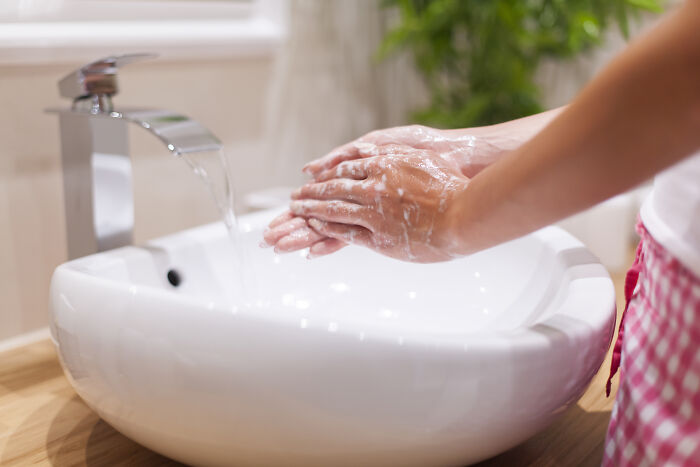 Person washing hands over a clean bathroom sink highlighting red flags in someone’s home hygiene and cleanliness.