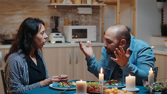 Couple having a tense dinner in a dimly lit kitchen, highlighting red flags that scream turn around and leave in someone’s home.