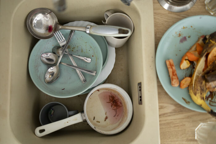 Dirty dishes piled in a kitchen sink with food scraps and utensils showing common red flags in someone’s home cleanliness.