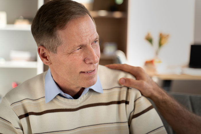 Middle-aged dad in a sweater receiving comfort at home, reflecting on surprise baby news and family challenges.