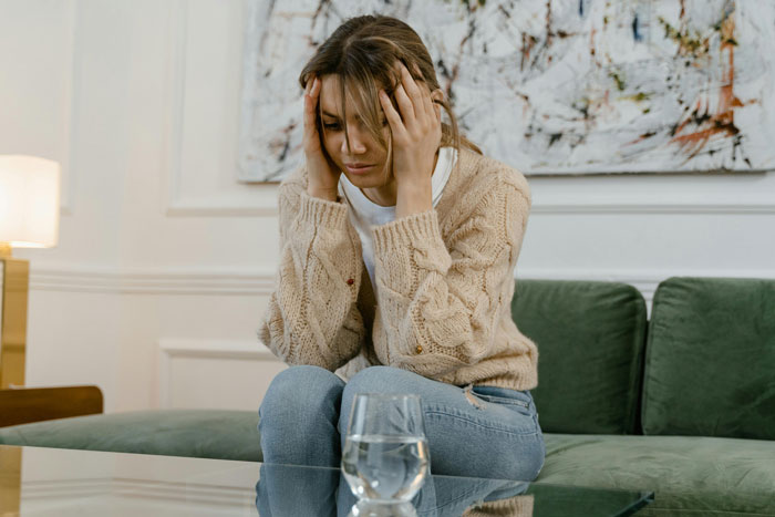 Sad young woman sitting on couch, upset and stressed, refusing to support dad and his mistress in wedding roles.