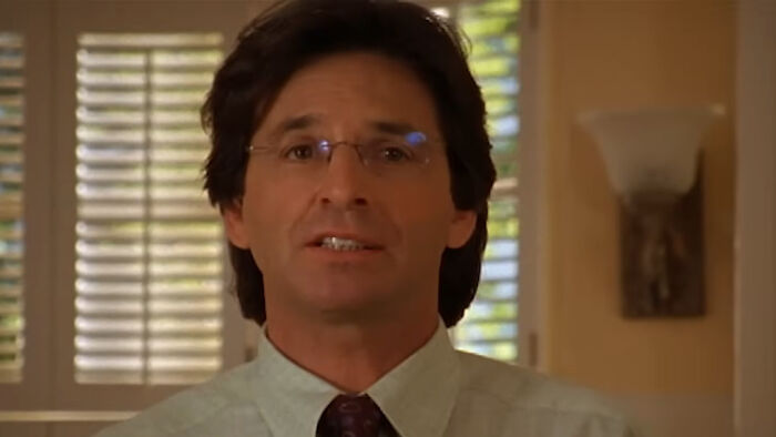 Man in glasses and a tie speaking indoors, related to Robert Carradine&rsquo;s passing and Disney Lizzie McGuire controversy.