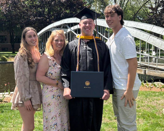 Family of trans mom Roberta Dorgan posing outdoors at a graduation ceremony near a white bridge in Rhode Island.