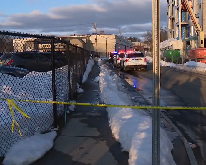 Police cars with flashing lights on a snow-lined street near a fenced area after Rhode Island hockey tragedy.