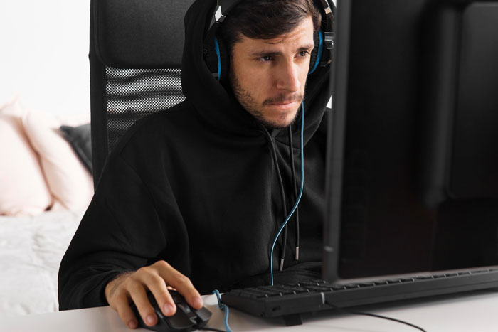Man focused on computer screen wearing headphones, sitting at desk, representing RuneScape gaming experience. - 6