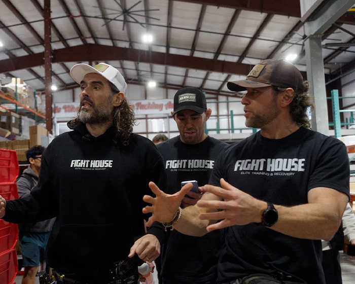 Russell Brand in casual attire with others, sparking outrage amid disturbing charges after hot tub baptisms.