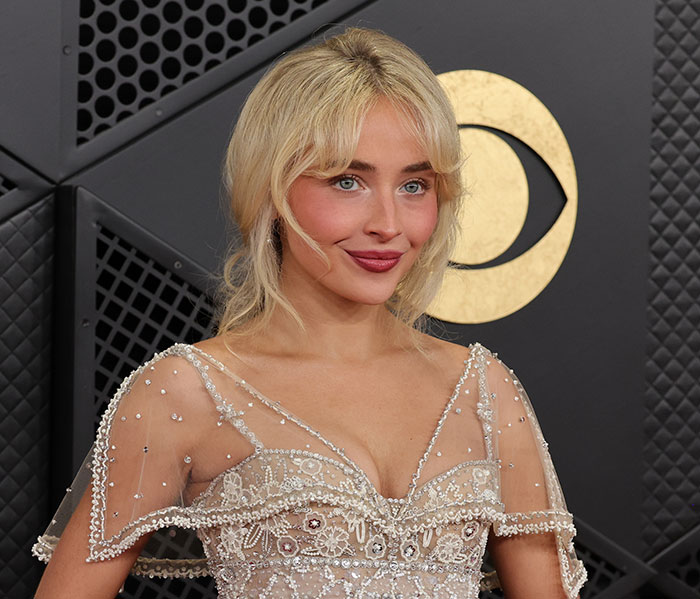 Sabrina Carpenter posing at an event, wearing a sheer beaded dress, amid controversy over her 2026 Grammys performance.