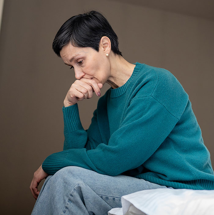 Woman wearing teal sweater sitting thoughtfully, reflecting on limits and autistic kids influencing motherhood decisions.