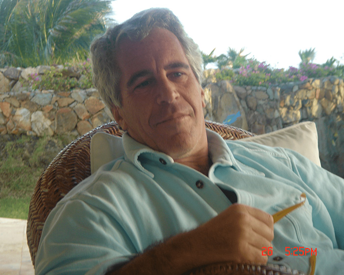 Epstein sitting outdoors in a light blue shirt, relaxed in a wicker chair with a stone wall and greenery background. Epstein sitting outdoors in a light blue shirt, relaxed in a wicker chair with a stone wall and greenery background.