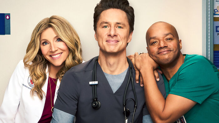 Cast members from Scrubs season 10 smiling together in medical attire on a hospital set, promoting the new episodes release. Cast members from Scrubs season 10 smiling together in medical attire on a hospital set, promoting the new episodes release.