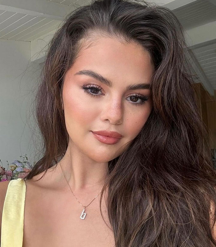 Selena Gomez with natural makeup and long hair in a casual indoor setting, related to Taylor Swift gift backlash.