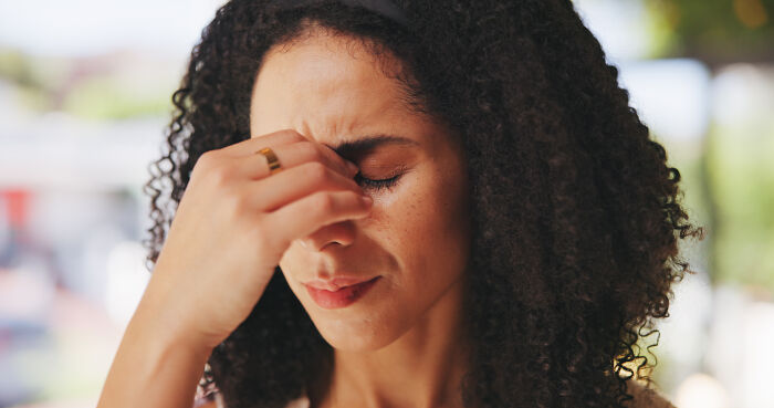 Woman with curly hair pinching the bridge of her nose, appearing frustrated while partner focuses on fourth hobby before breakfast.