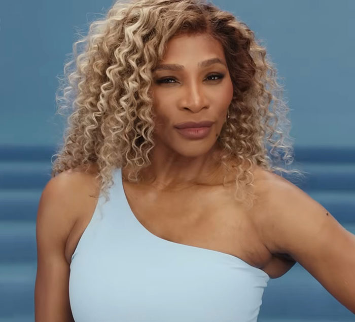 Serena Williams posing with curly blonde hair and wearing a light blue top amid controversial weight loss transformation debate.
