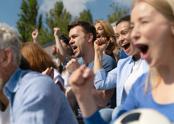 A crowd of people cheering passionately outdoors, showing enthusiasm and confidence with raised fists and excited expressions.
