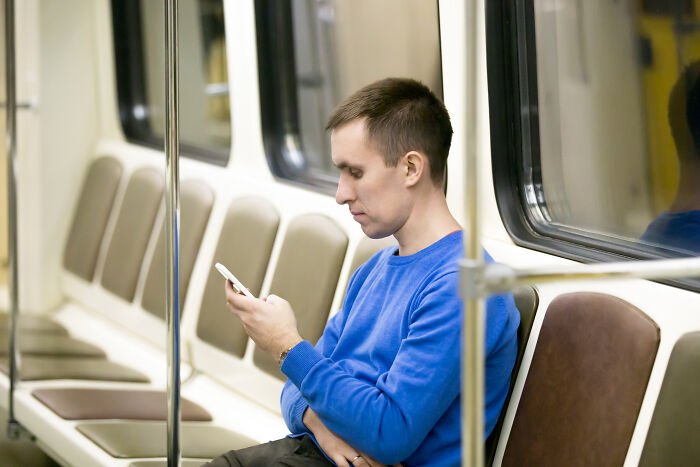 Man in blue sweater using phone alone on subway, illustrating signs of very low intelligence in a public setting.