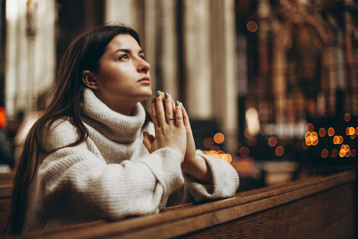 Young woman in a cozy sweater praying inside a church, reflecting on signs of very low intelligence and behavior.
