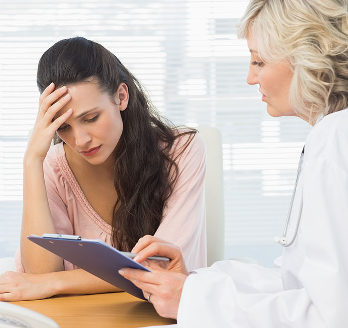 Woman looking stressed while doctor explains notes on a clipboard, illustrating signs of very low intelligence.