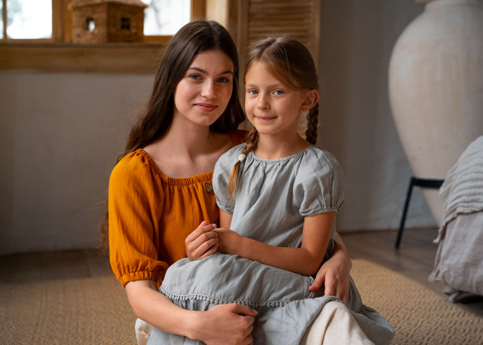 Young sister and child sitting together indoors, sharing a calm moment despite family parenting drama challenges.