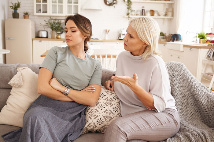 Two women having a serious sister family parenting drama conversation on a couch in a cozy living room.