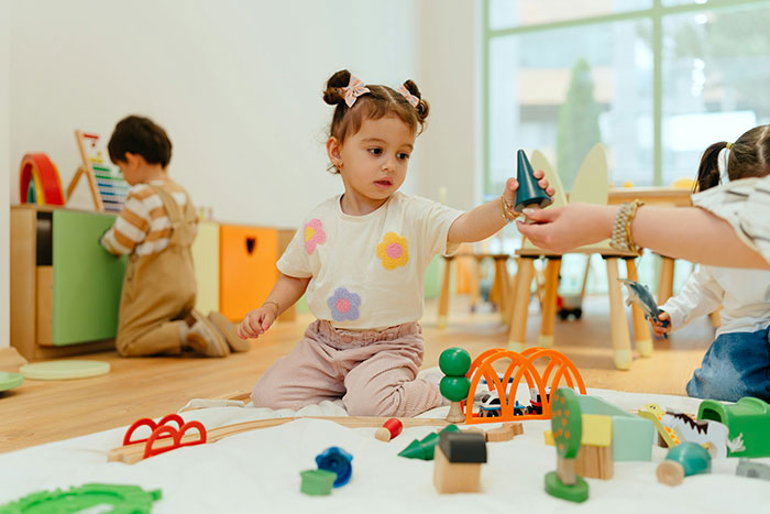 Toddler girl playing with toys and handing a cone to another child, illustrating family dynamics and favors theme.